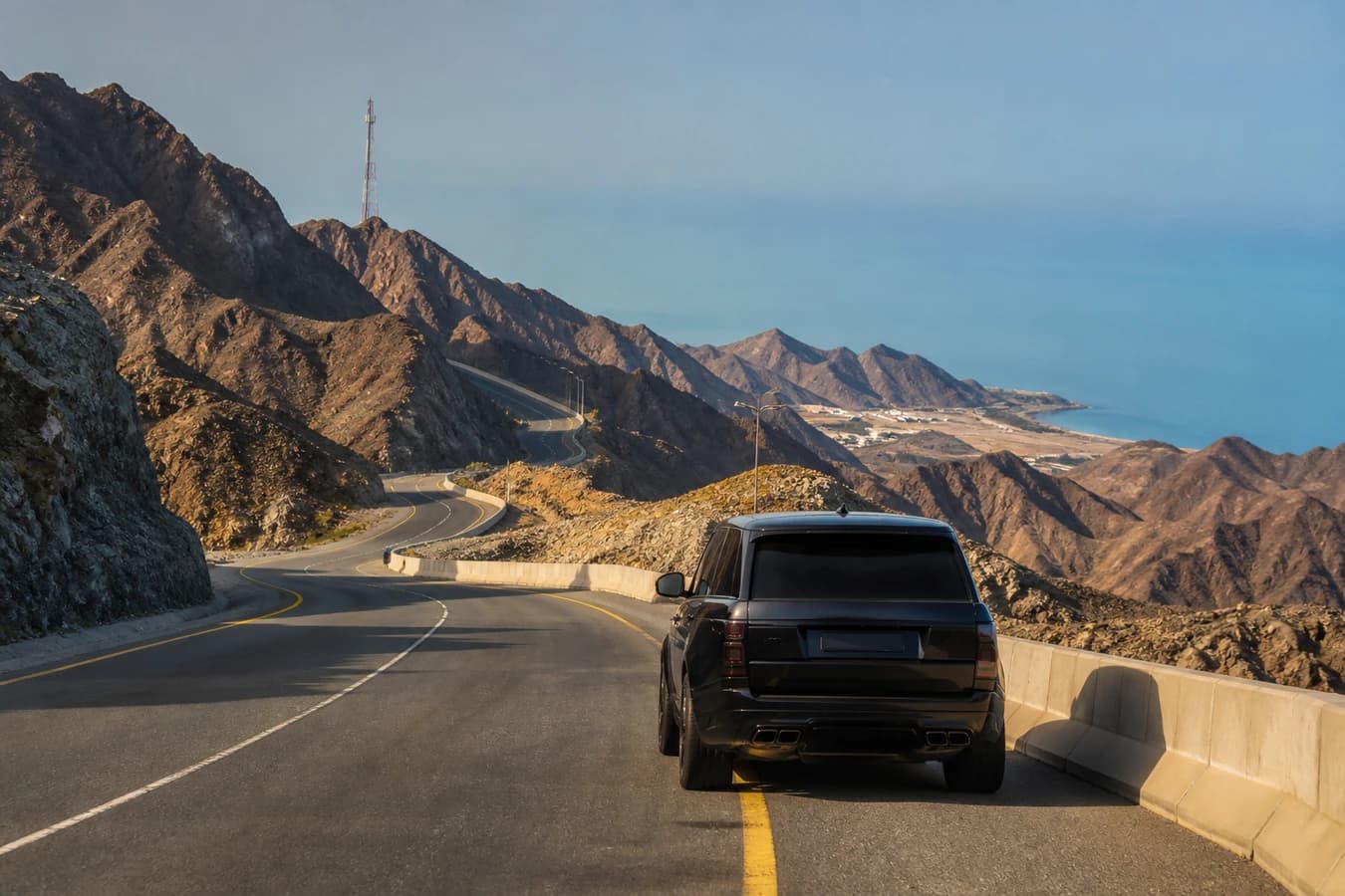 Dubai to Fujairah luxury car road trip: luxury SUV on an east-coast mountain highway with sea beyond
