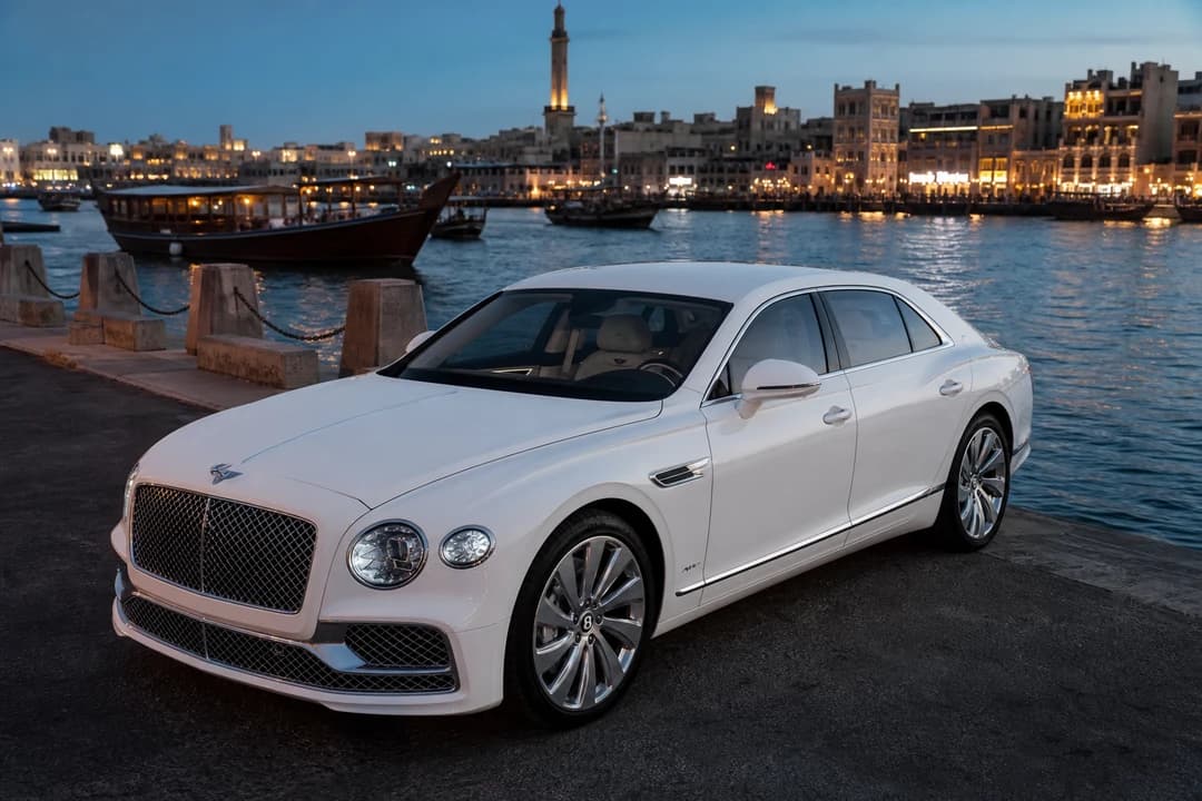 Bentley Continental GT on Dubai Creek in Deira at blue hour with wooden dhows for UAE road trip rental evenings