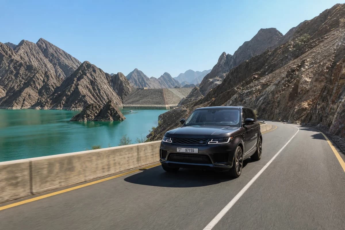 Luxury SUV on winding UAE tarmac road with Hajar mountain scenery for Dubai road trip