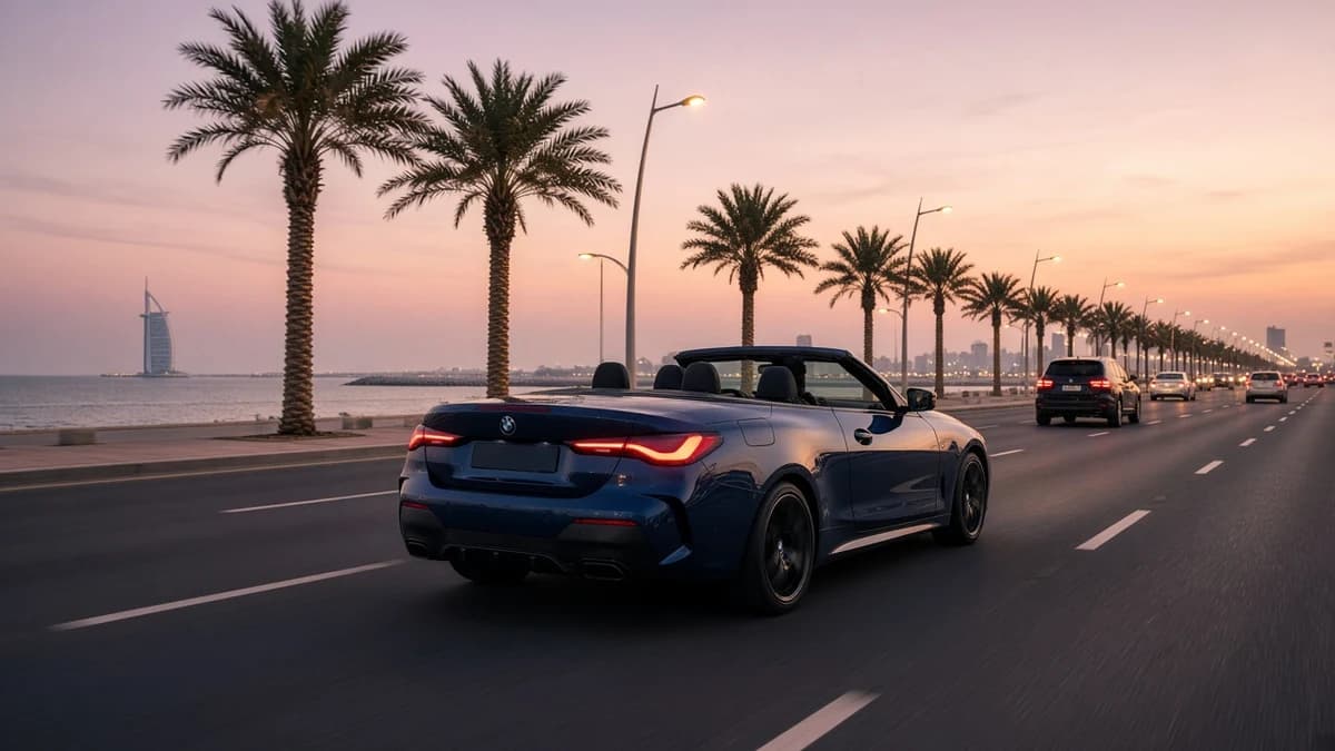Dark blue BMW 4 Series Convertible driving in the right-hand lane of a palm-lined Dubai coastal road at dusk