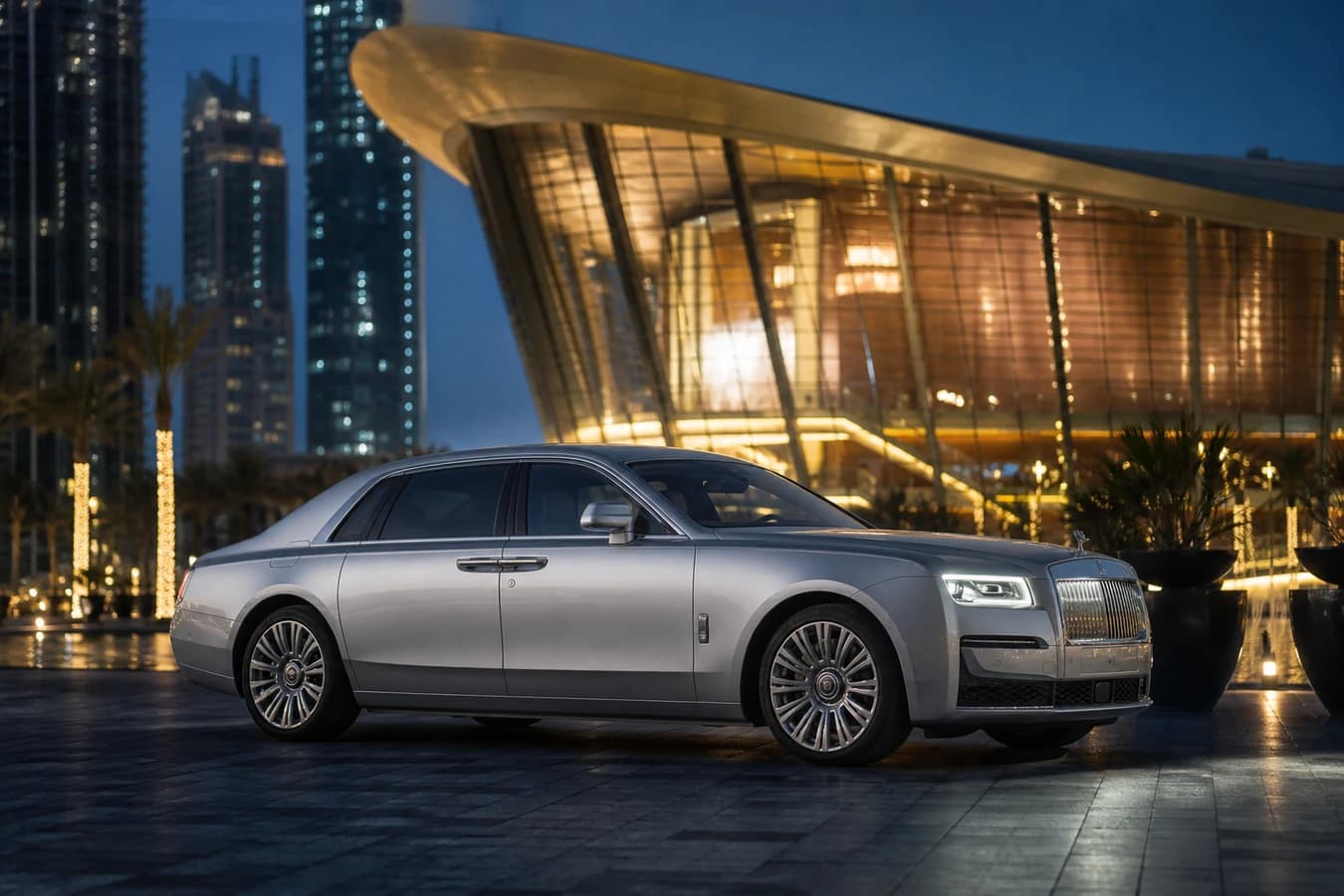 Dubai Opera luxury car rental: silver Rolls-Royce Ghost at Dubai Opera plaza at blue hour