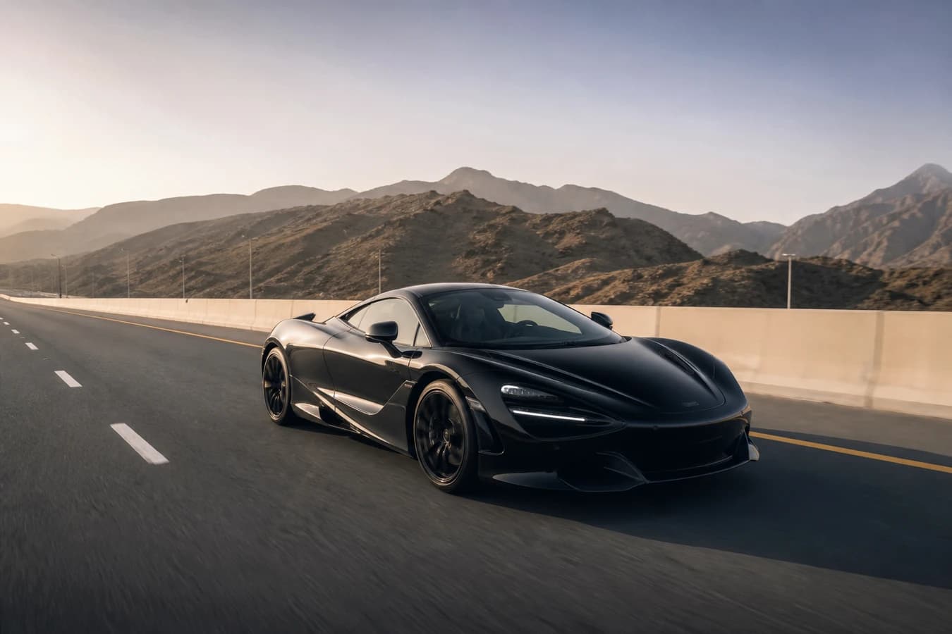 Dubai to Ras Al Khaimah supercar: low exotic coupe on a northern UAE dual carriageway toward the Hajar foothills