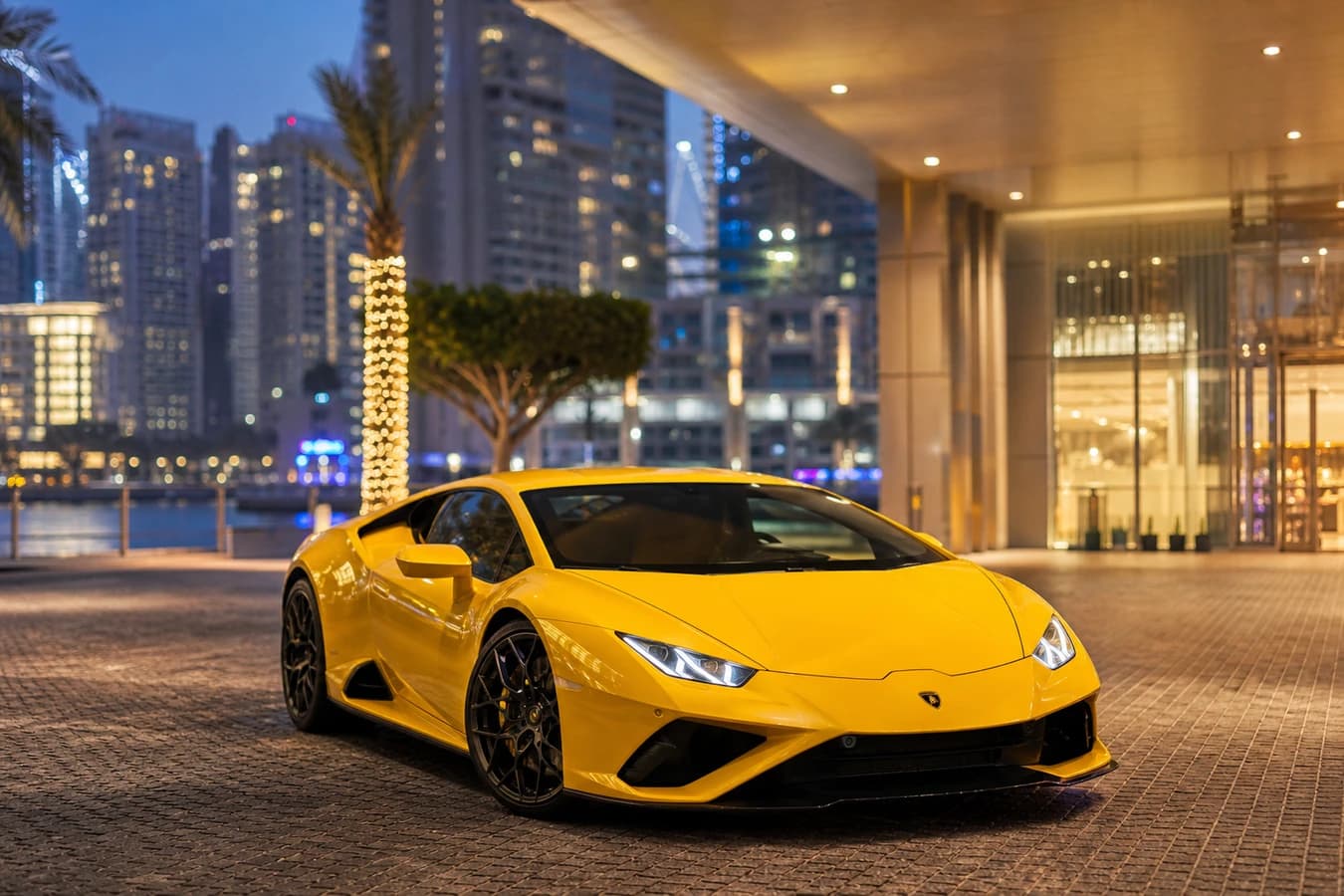 Festive season supercar rental Dubai: yellow Huracán at a Marina hotel porte-cochère during peak winter evenings