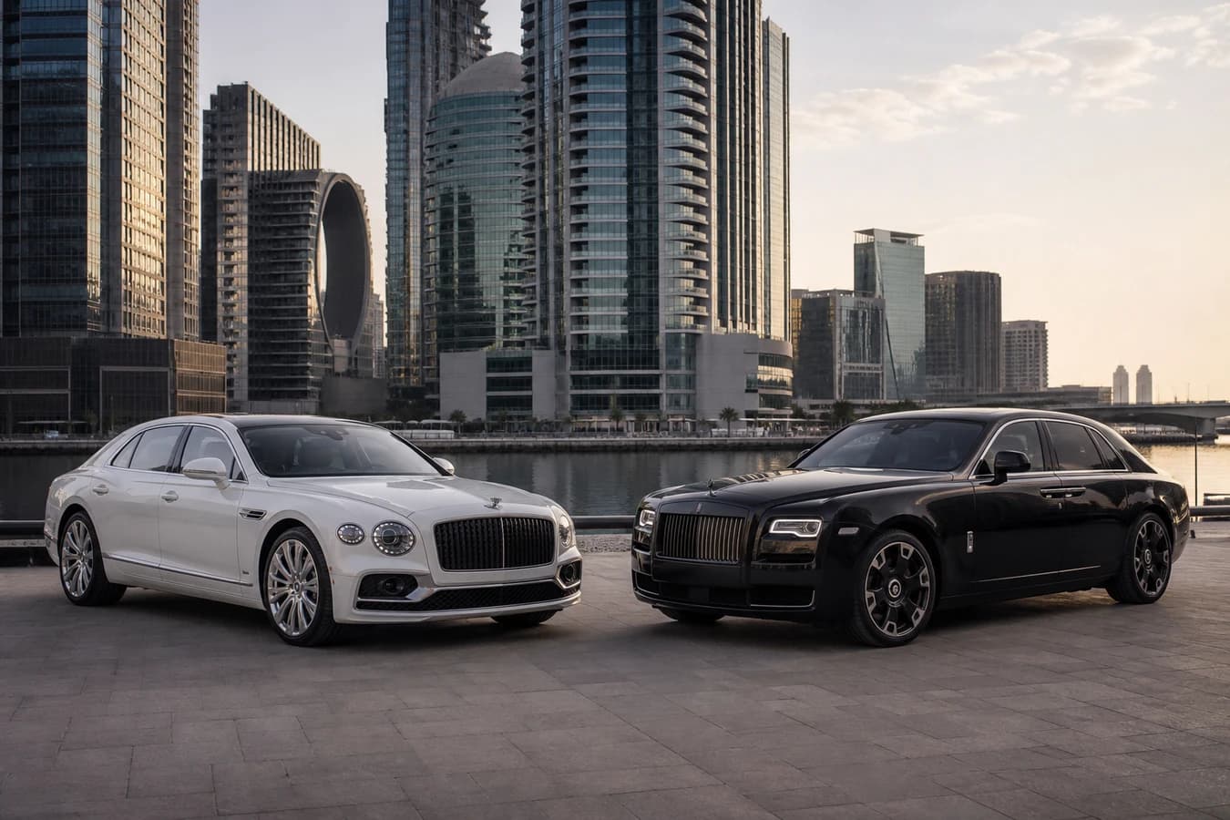 Flying Spur vs Ghost rental Dubai: white Bentley Flying Spur and black Rolls-Royce Ghost at Business Bay canal in morning light