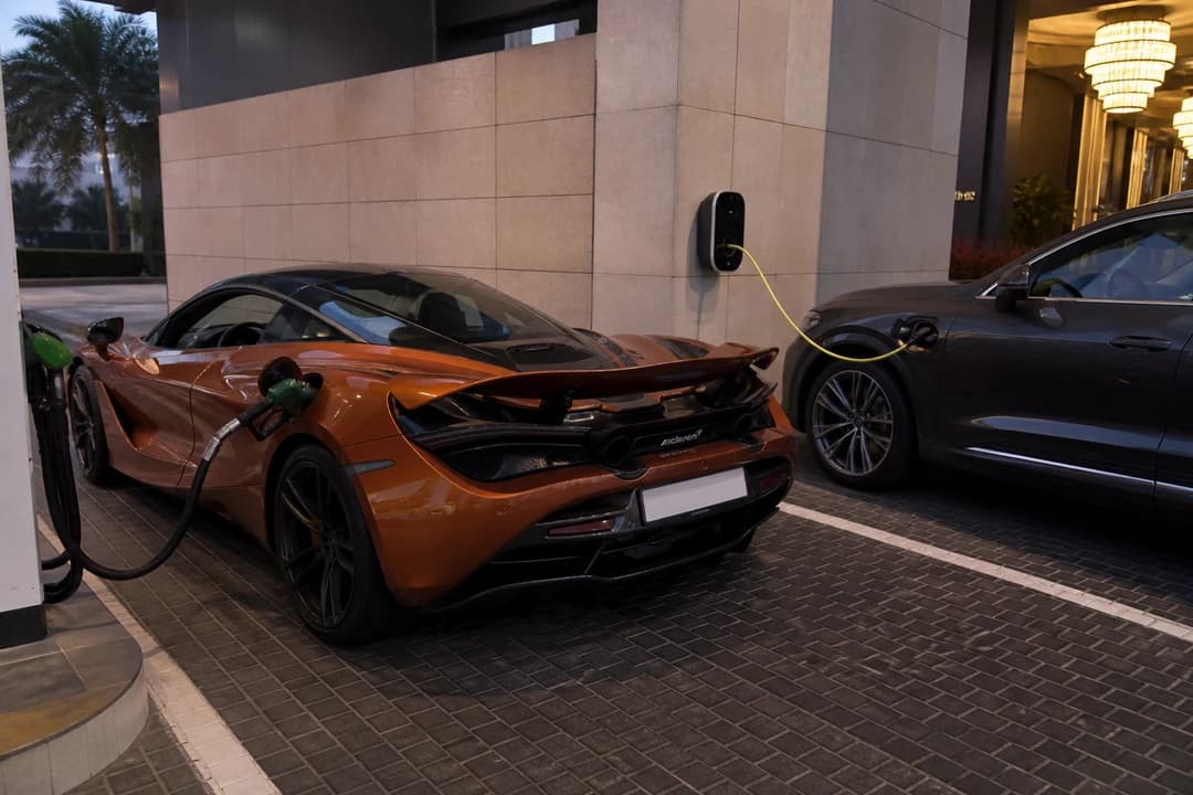 Petrol pump beside a McLaren and a hybrid charge cable at a Dubai hotel bay for luxury car hire Dubai energy planning