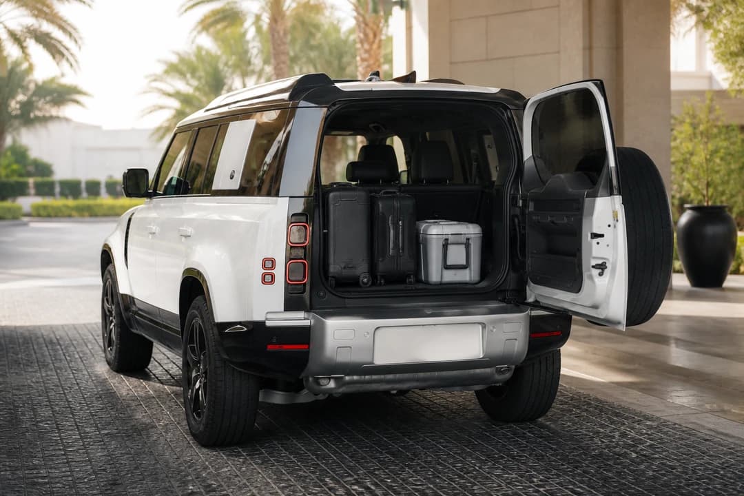 Defender 110 boot loaded with soft roller cases and a cooler at a Dubai hotel driveway for luxury car rental Dubai packing