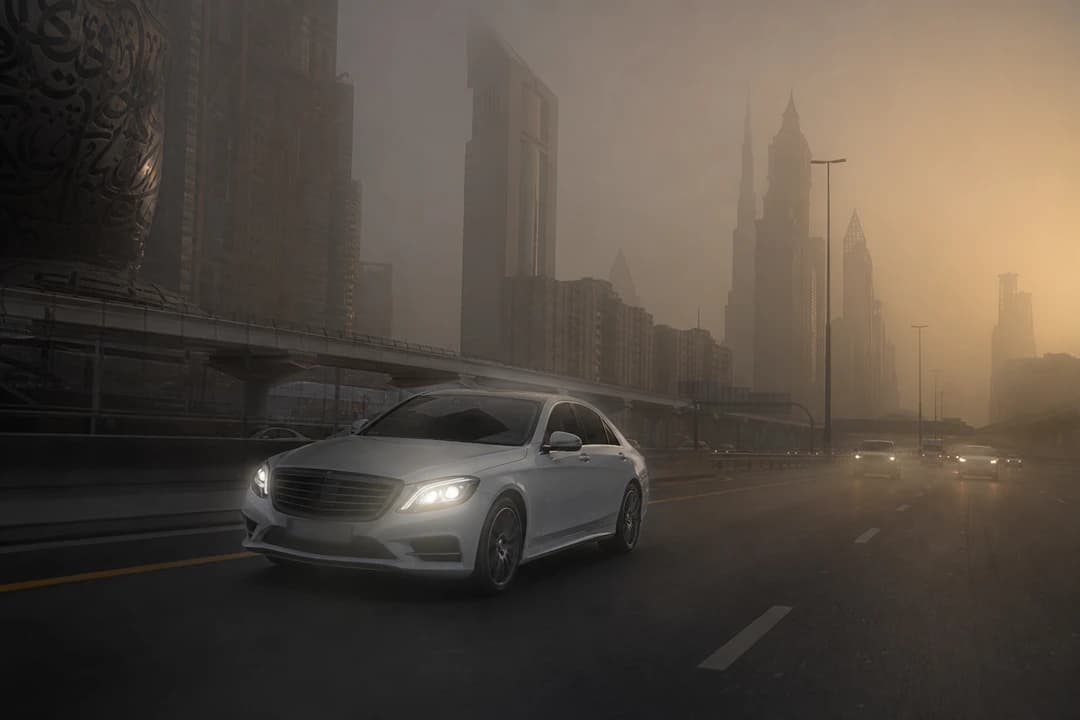 Dubai driving rules in dusty weather: white luxury sedan with low-beam lights on Sheikh Zayed Road during a dust haze