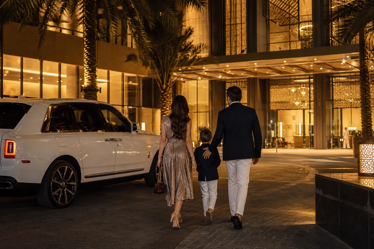 Family walking from a Rolls-Royce Cullinan to a Mall of the Emirates hotel entrance at night